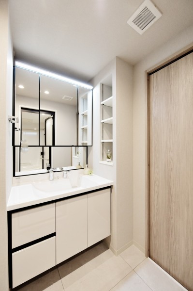 大きな三面鏡で身だしなみを整えやすい洗面台です。タッチレススイッチで手を触れずに照明をオンオフでき、清潔に使用できます。壁に棚を設置し、小物類の整頓にも便利です。