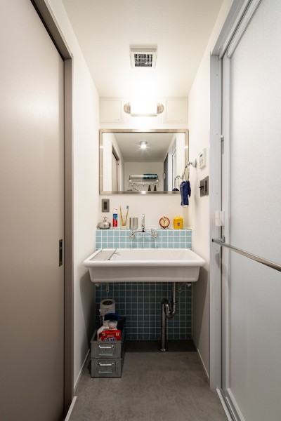 落ち着きのあるリビングダイニングと比べ、洗面室は水色のタイルがアクセントになった清潔感のある明るい空間に仕上げました。洗面台の照明、ミラー、タオルリングもダルトン製。