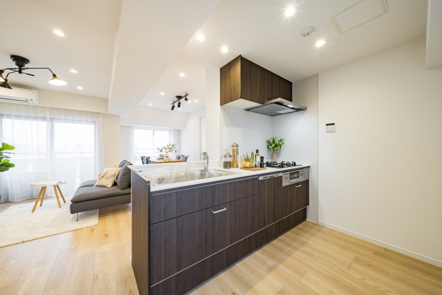 キッチンからリビングまで視線が抜けるシームレスな空間設計です。リビングの白とコントラストをなす落ち着いたダークカラーの木目調のシステムキッチンは、空間に上質感をもたらします。